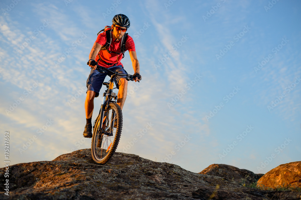 Cyclist in Red Riding the Bike Down the Rock on the Blue Sky Background. Extreme Sport and Enduro Biking Concept. Cyclist in Red Riding the Bike Down the Rock on the Blue Sky Background. Extreme Sport and Enduro Biking Concept.