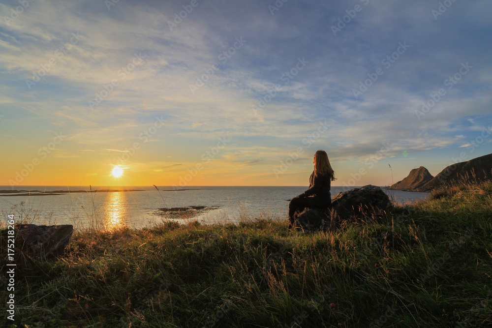 Woman watching the sunrise, view from Vaeroy island, Lofoten, Norway