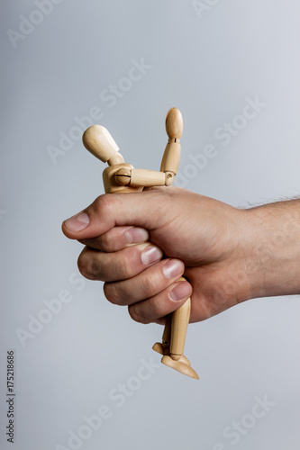 male hand gripping a stick figure of a wooden man. Stick person folded.