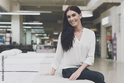 A woman chooses a mattress in a store. She sits on it and examines it. Free Download A woman chooses a mattress in a store. She sits on it and examines it. - GFXLoad
