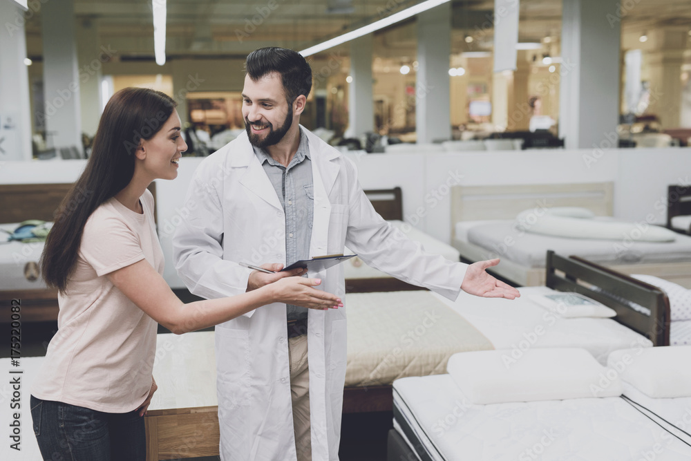 Consultant-orthopedist helps the girl to choose a mattress in the store. He interrogates a woman Consultant-orthopedist helps the girl to choose a mattress in the store. He interrogates a woman