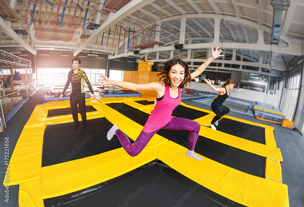 Cheerful and happy woman practicing and jumping on trampolines in a sports indoor center, workout and modern entertainment concept - obrazy, fototapety, plakaty 