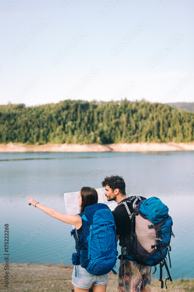 Hiking couple. Young couple with backpacks looking at the map beside lake