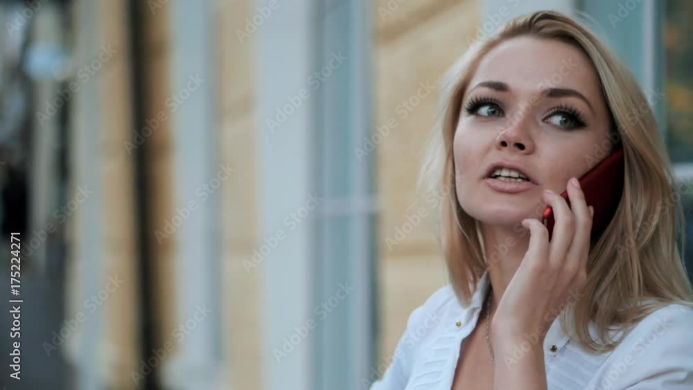 Young beautiful blonde businesswoman talking by cellphone in the city. Woman wearing white shirt. Slow motion. Young beautiful blonde businesswoman talking by cellphone in the city. Woman wearing white shirt. Slow motion.
