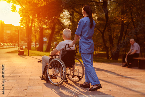 Nurse and old man who sits in a wheelchair watching the sunset in the park photo