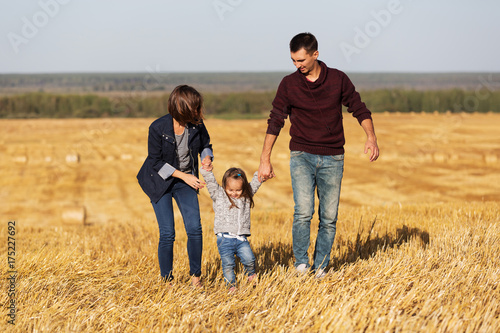 Happy young family with 2 year old girl walking in a harvested field