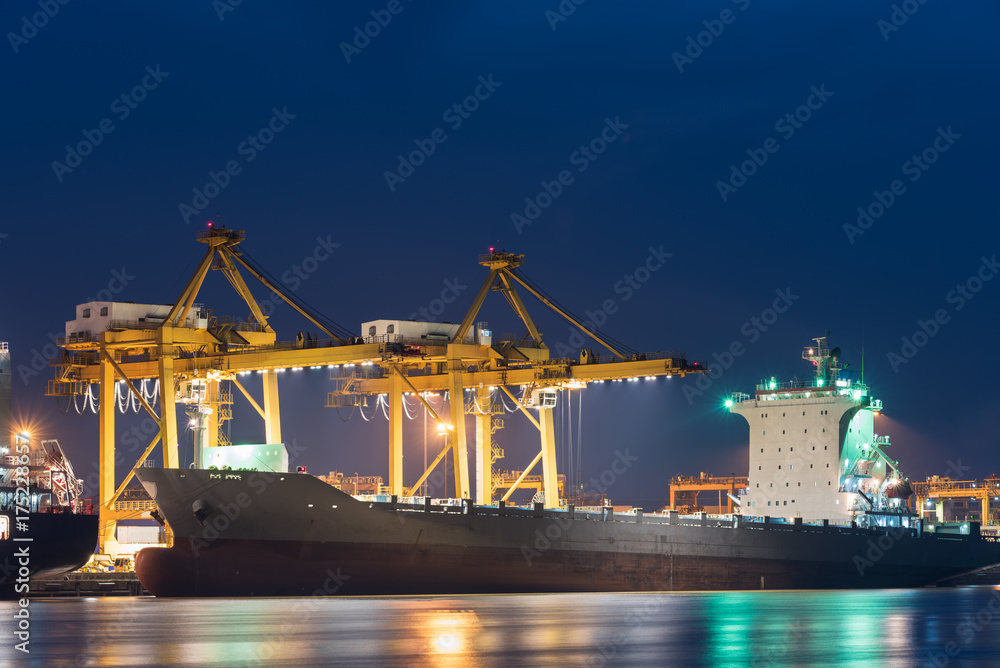 container cargo freight ship with working crane bridge in shipyard at twilight