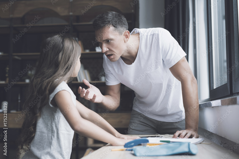 Obraz premium The father in a white T-shirt screams at his little dark-haired daughter, who stands next to him near the pine table