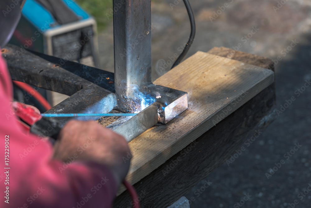 A man welds a metal product with arc welding machine, lots of smoke, bright lights and sparks