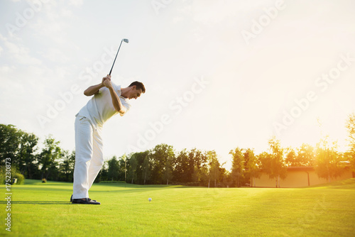 A man in a white suit plays golf. He took the stick and was preparing to strike
