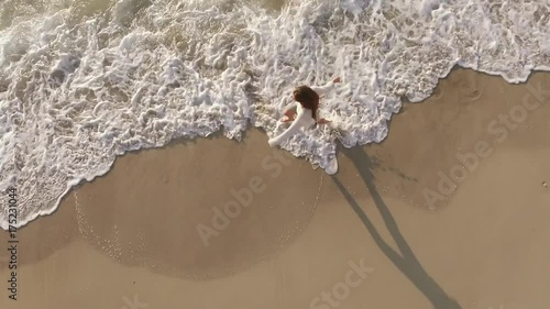 view from above cheerful nice girl with long hair barefoot running along seaside looking up at camera with smile at dawn rapid footage  photo