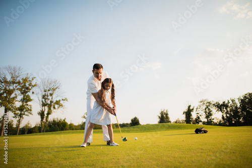 First hit. A man teaches his daughter to play golf and the girl with his help made the first golf club
