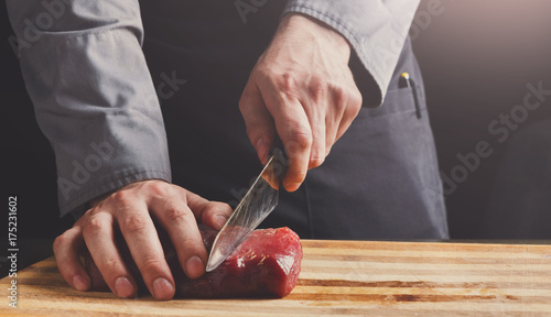 Chef cutting filet mignon on wooden board at restaurant kitchen