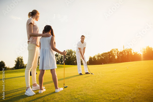 Family playing golf at sunset. A woman and a girl are looking at a man who is preparing to make a hit