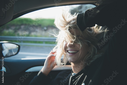 Young blonde woman in the car with the window open. The wind moves her hair.