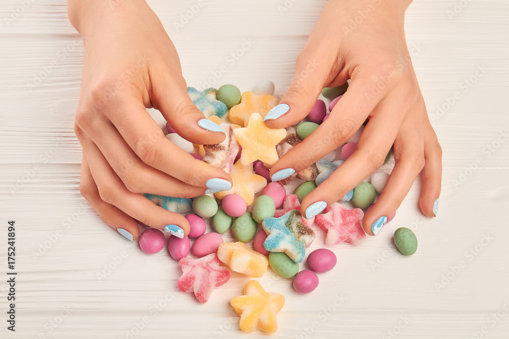 Female hands and colorful candies. Woman manicured hands and multicolored tasty candies on white wooden background close up. Female hands and colorful candies. Woman manicured hands and multicolored tasty candies on white wooden background close up.