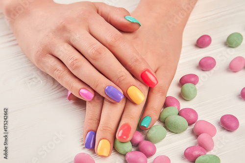 Multicolored manicure and candies close up. Female hands with stylish colorful nails and multicolored candies on white wooden background close up.