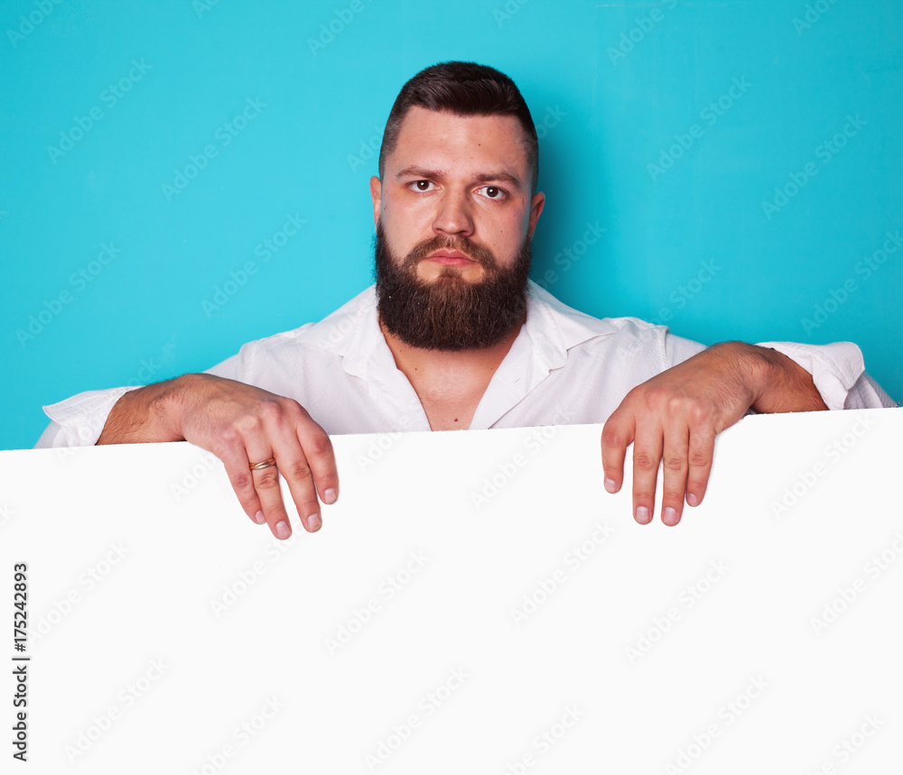 handsome young man with long beard and moustache on face with pointing finger on blue background in studio, copy space handsome young man with long beard and moustache on face with pointing finger on blue background in studio, copy space