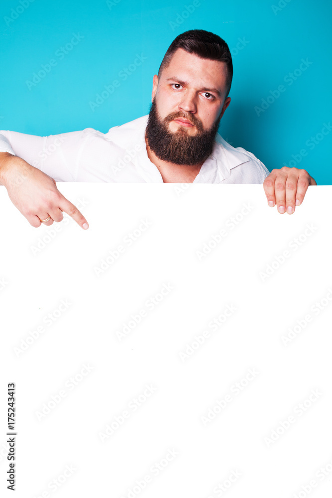 handsome young man with long beard and moustache on face with pointing finger on blue background in studio, copy space handsome young man with long beard and moustache on face with pointing finger on blue background in studio, copy space