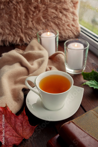 A cup of tea, autumn leaves, a blanket, candles, books on a table near the window of a rainy weather photo