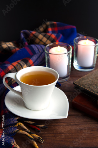 A cup with a hot tea drink on a wooden background with an autumn plaid, cones, photo
