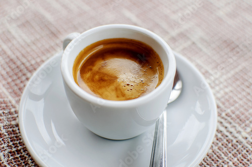 A cup of freshly prepared espresso coffee with foam on fabric  horizontal image