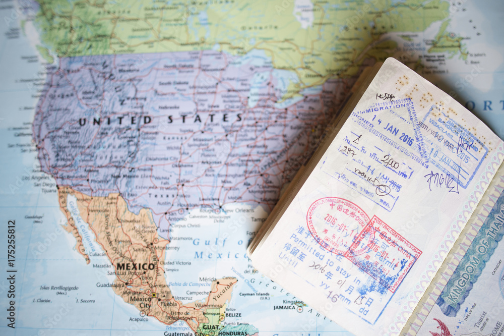(Selective focus) Close-up view of a passport with entry stamps on a blurred geographical map of the world. The map shows the United States an Mexico
