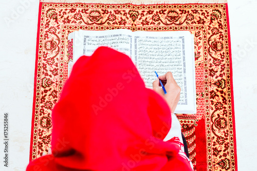 Asian Muslim woman reading Koran or Quran on praying carpet wearing traditional dress