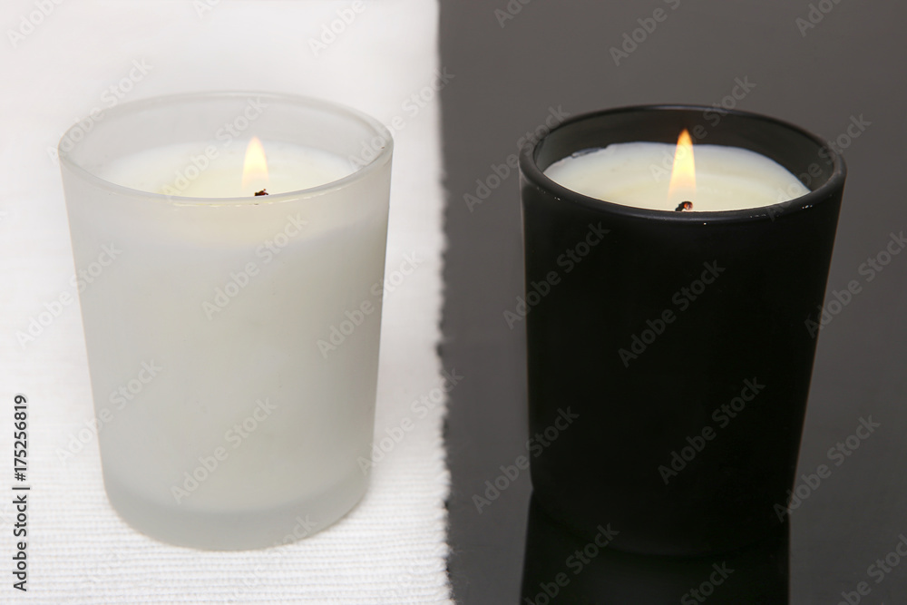 White and black candles. Two burning candles on black table with white napkin. White and black candles. Two burning candles on black table with white napkin.
