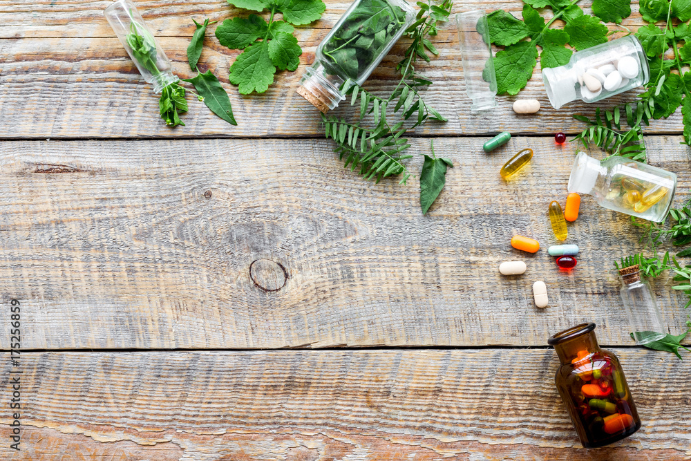 Homeopathy. Leaves of healing herbs, bottles and pills on wooden background top view copyspace Homeopathy. Leaves of healing herbs, bottles and pills on wooden background top view copyspace
