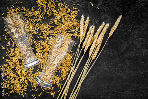 Grains and ears of malting barley near beer glass on black background top view copyspace