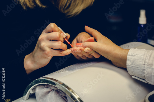 Manicurist applying red nail varnish. Manicure master painting female finger with close up. Manicure and fingers care. photo