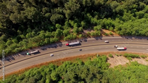 Cinematic, dizzying, spinning motion camera move, a bird's eye view of freeway traffic passing through a forest area.