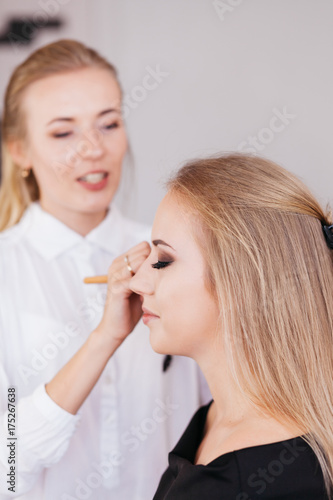 Professional makeup artist working with beautiful young woman in black dress