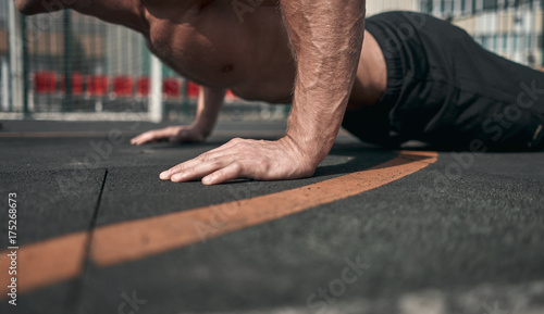 Close-up. Athletic man presses from the floor. Outdoors. Green colors. Sports ground.