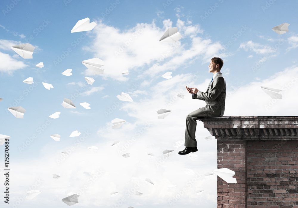 Man on roof edge send message with smartphone and cityscape at background Man on roof edge send message with smartphone and cityscape at background