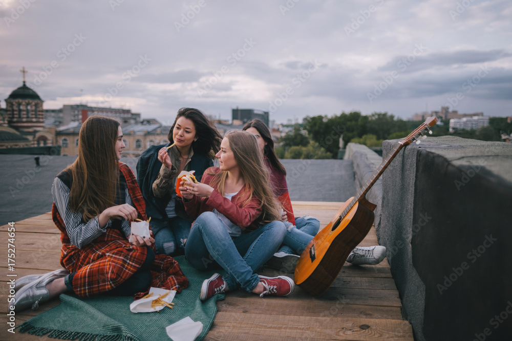 Acoustic guitar music and meeting friends on roof. Smiling girls with fast food, unusual places for rest and communication, sharing time together, cheerful and joyful atmosphere concept