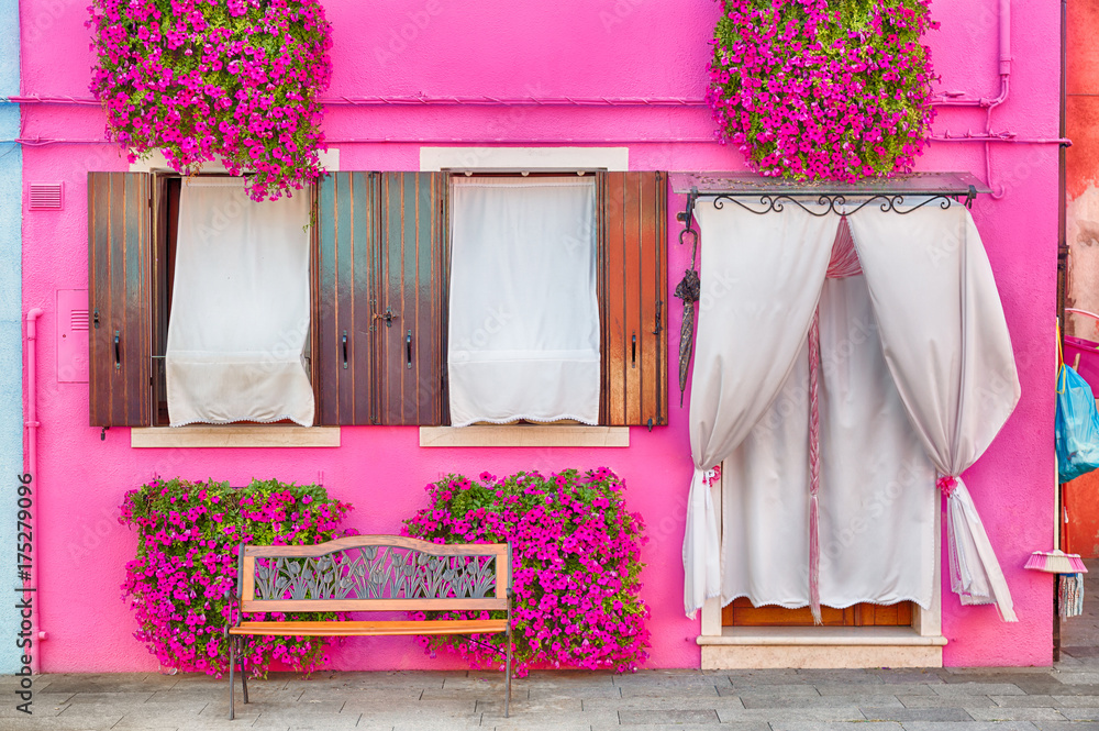 Fototapeta premium Różowy dom z różowymi kwiatami i roślinami. Ładna ławka pod oknami. Kolorowy dom w Burano wyspie blisko Wenecja, Włochy