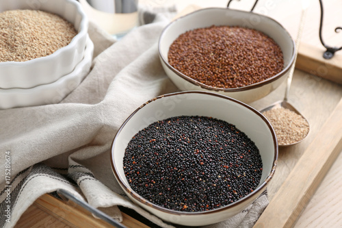 Bowls with different quinoa seeds on wooden tray