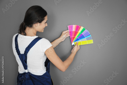 Female decorator holding color palette samples against grey background