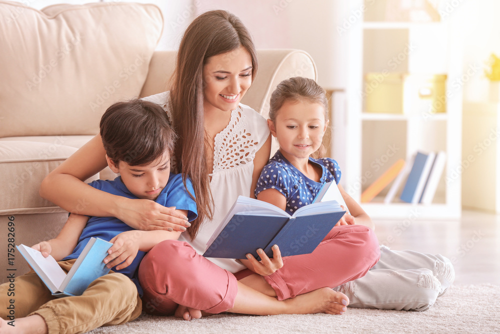 Fototapeta premium Young woman and her little children reading books at home