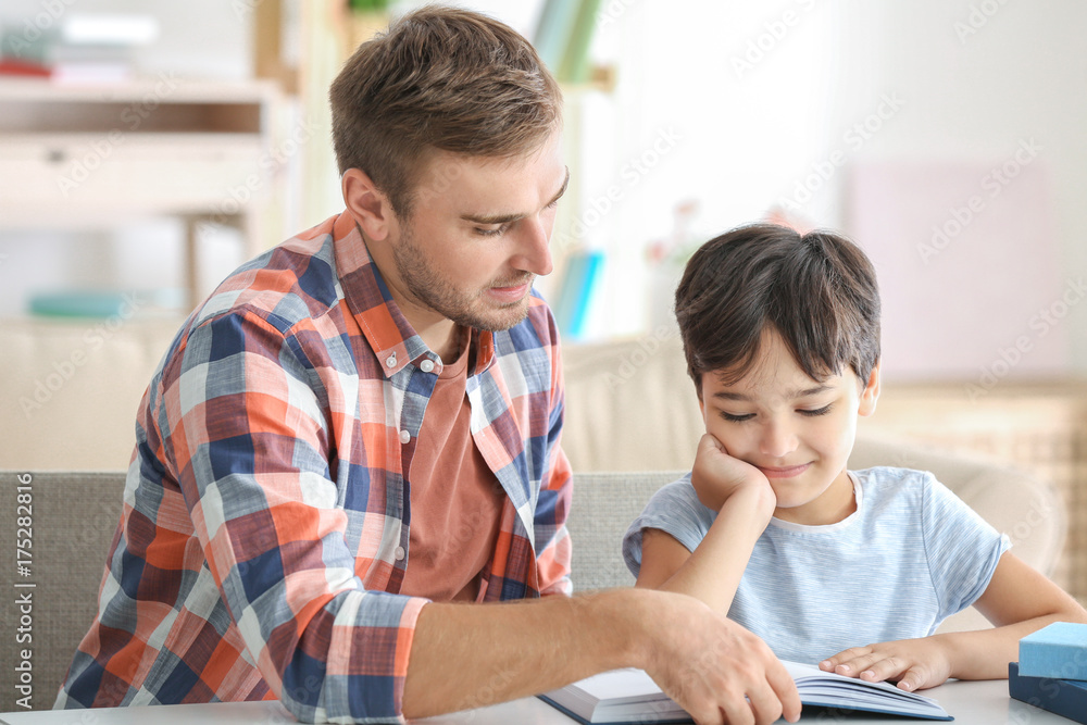 Young man and his little son reading book at home Young man and his little son reading book at home
