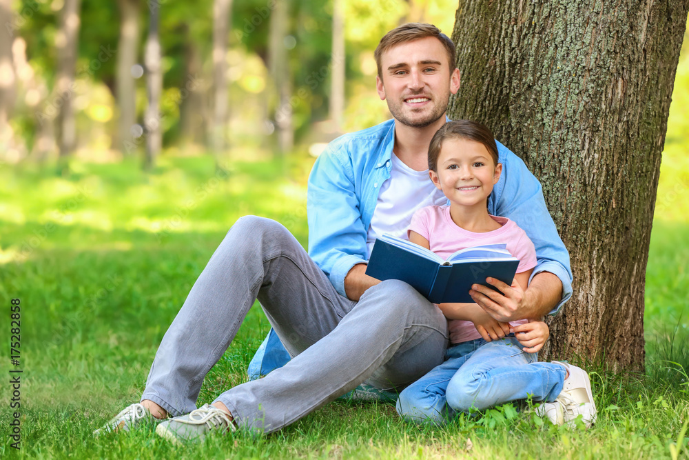 Young man and his little daughter reading book in park Young man and his little daughter reading book in park