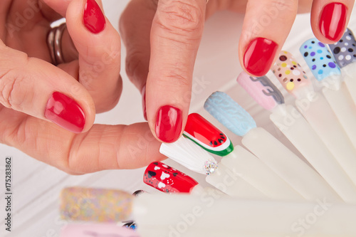 Close up of female hands and nail art samples. Senior woman hands with red manicure holding plastic tips with nail art design. Woman choosing nail design close up.