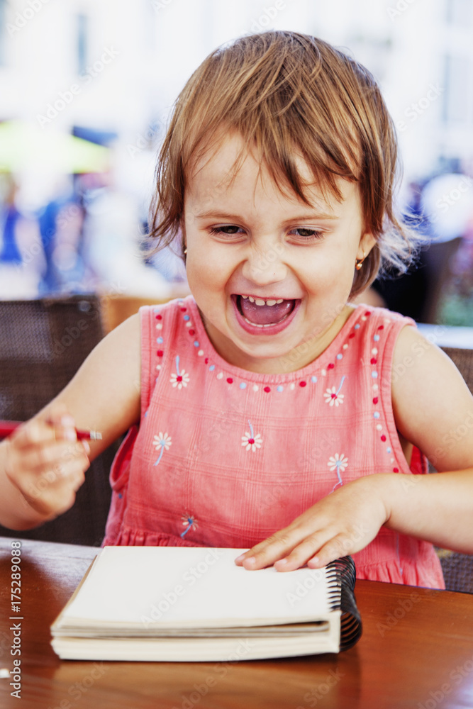 Little beautiful child girl laughing and writing a letter. Emotional facial expressions. (Education, studies, success, happy childhood concept) Little beautiful child girl laughing and writing a letter. Emotional facial expressions. (Education, studies, success, happy childhood concept)