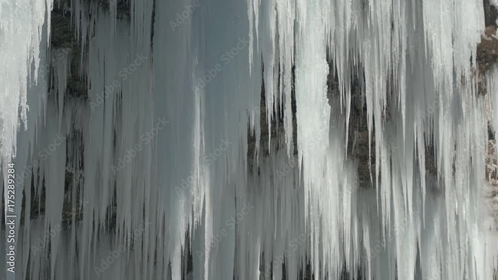 CLOSEUP Winter river cascade frozen into white sparkling icicles. Stunning frost icicles hanging from rocky mountain cliff on winter day Early spring sun melting icy waterfall water drops dropping off CLOSEUP Winter river cascade frozen into white sparkling icicles. Stunning frost icicles hanging from rocky mountain cliff on winter day Early spring sun melting icy waterfall water drops dropping off