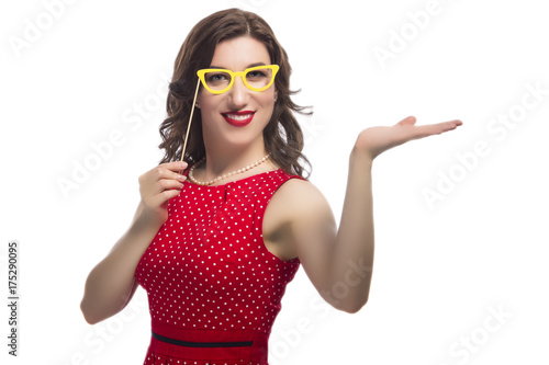 Youth Lifestyle Concept and Ideas. Portrait of Smiling Caucasian Female with Color Paper Artistic Spectacles In Front Of Face.Posing with Lifted Hand Against Pure White.