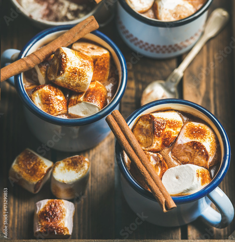Hot chocolate in enamel mugs with cinnamon and roasted marshmallows in wooden tray, selective focus, square crop
