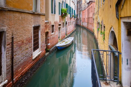 Small boat on a narrow canal surrounded by old weathered buildings in Venice