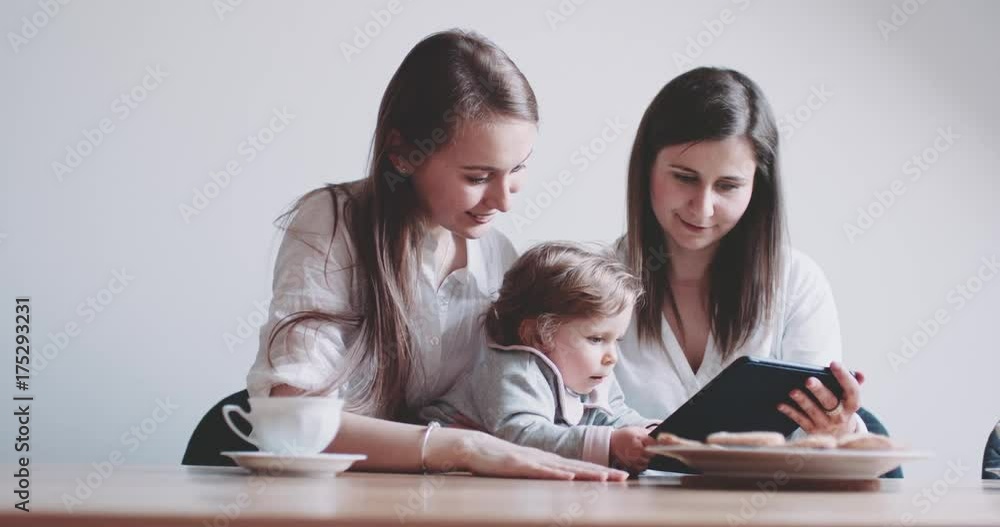 Two Women working on Laptop and sharing coffee, holding baby girl. Slow Motion 120 fps 4K DCi. Showing a computer to a child. Working from home. Generation Y. Sisters searching internet. Two Women working on Laptop and sharing coffee, holding baby girl. Slow Motion 120 fps 4K DCi. Showing a computer to a child. Working from home. Generation Y. Sisters searching internet.